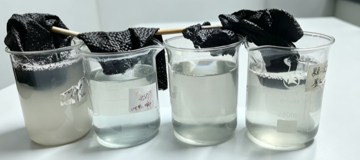 High color-fastness acid dyeing: black nylon fabric samples in beakers of dye liquor on a lab bench